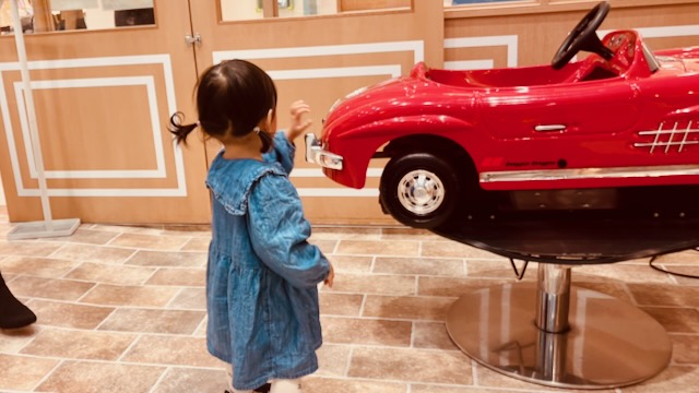 チョッキンズ店内で赤い車型チェアをのぞき込む1歳の下の子
